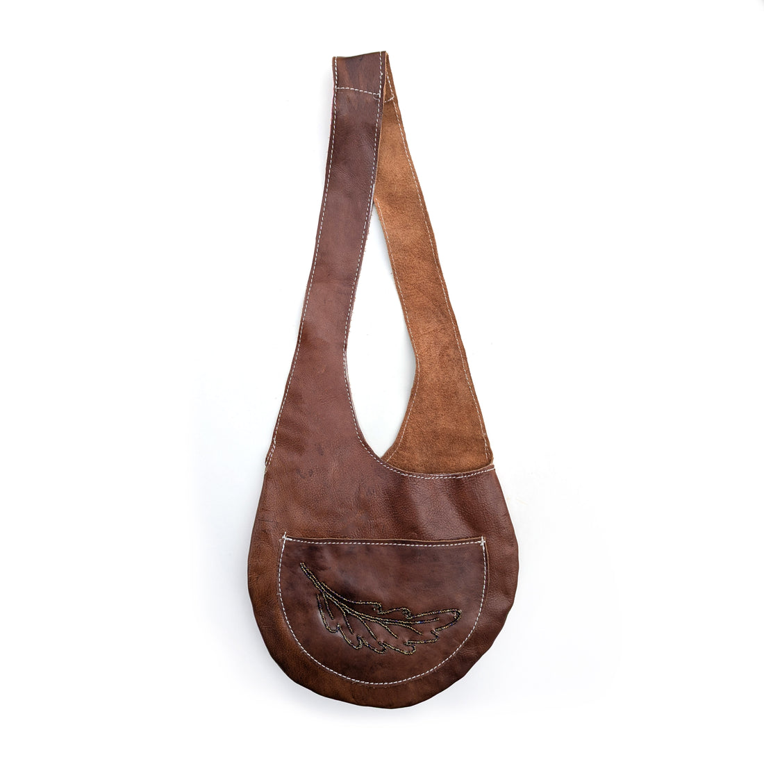 Brown leather sling bag with brown rainbow beaded fern design on white background.