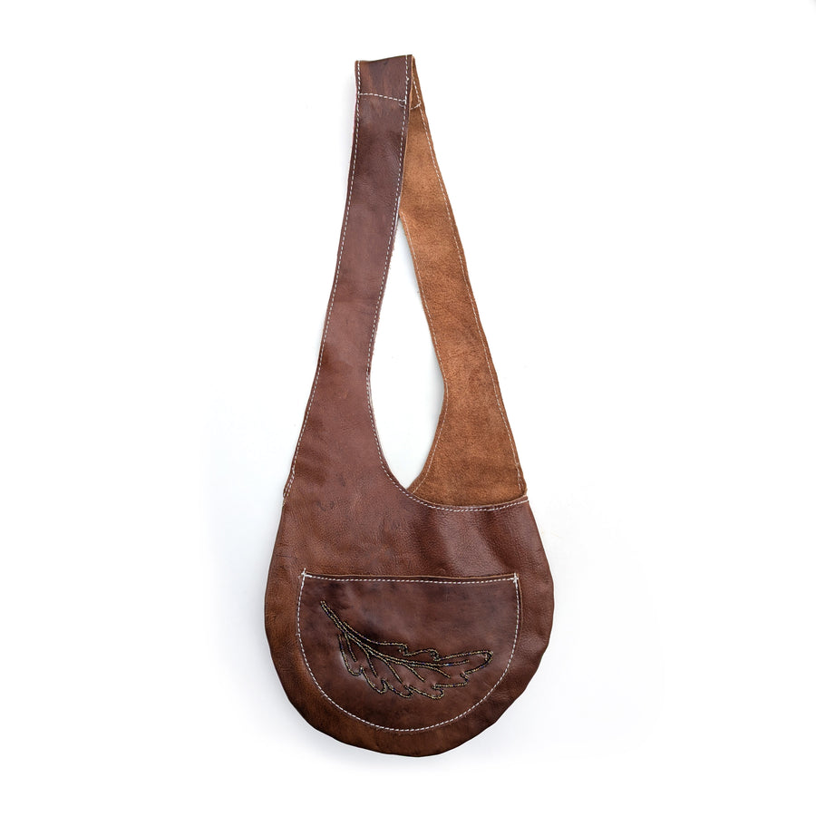 Brown leather sling bag with brown rainbow beaded fern design on white background.