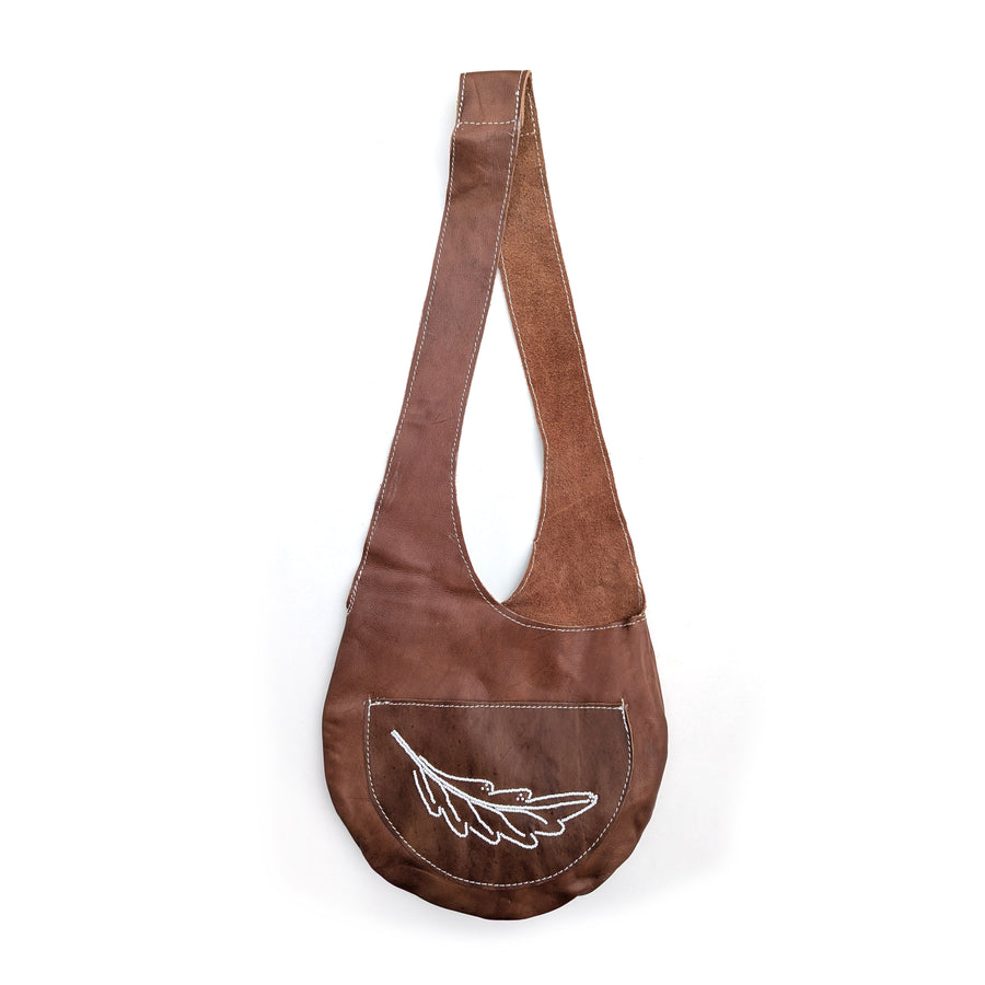 Brown leather sling bag with white beaded fern design on white background.