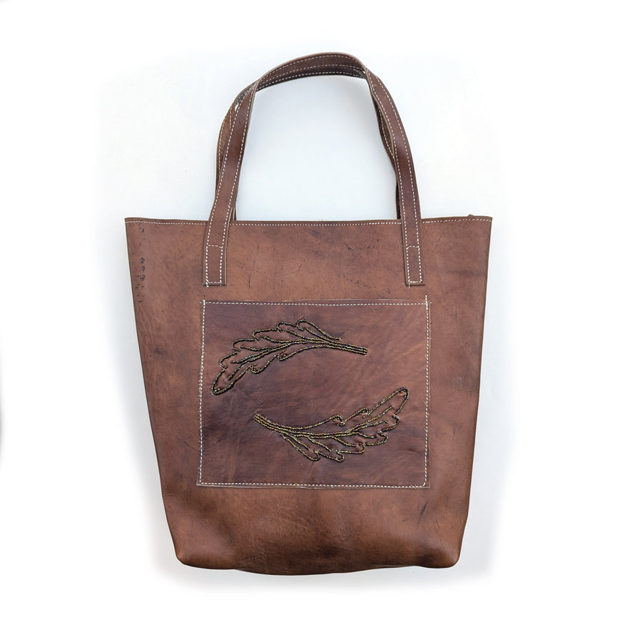 Leather tote bag with front pocket and brown rainbow beaded fern leaf design.