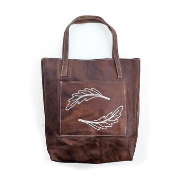 Leather tote bag with front pocket and white beaded fern leaf design.