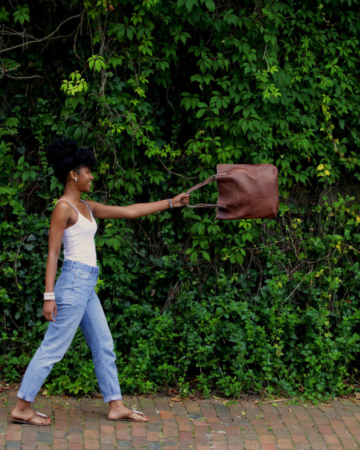 Woman walking with a brown bag against a green leafy background